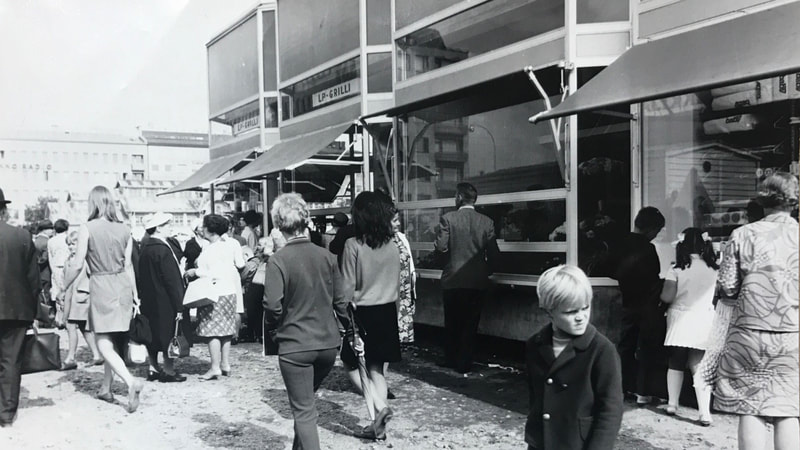Tuomiston kauppahallin erikoisuus oli myös se, että myyntiä tapahtui sekä hallin sisällä että ulkona julkisivuille sijoitettujen kioskien ja grillien kautta. Kuva kauppahallin avajaisten aikoihin vuodelta 1968. Kuva Pohjois-Karjalan museo.