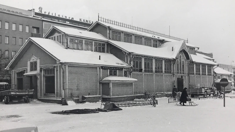 Ajoittamaton kuva (todennäköisesti 1960-luvun lopusta tai 1970-luvun alusta sillä taustalla näkyy Sokos-tavaratalo, joka valmistui 1968) ensimmäisestä kauppahallista torin pohjoislaidalla. Kuva Pohjois-Karjalan museo.